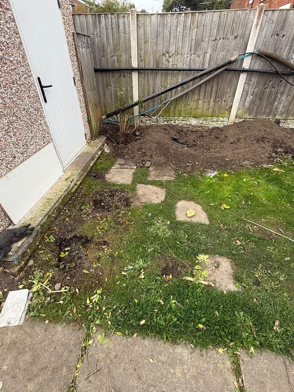 The worn lawn in Gwersyllt with sunken stepping stones and soil heaped against the fence before the work