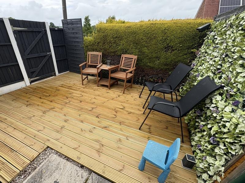 Golden pressure-treated timber decking with garden chairs beside a black fence and gate in Coedpoeth, Wrexham