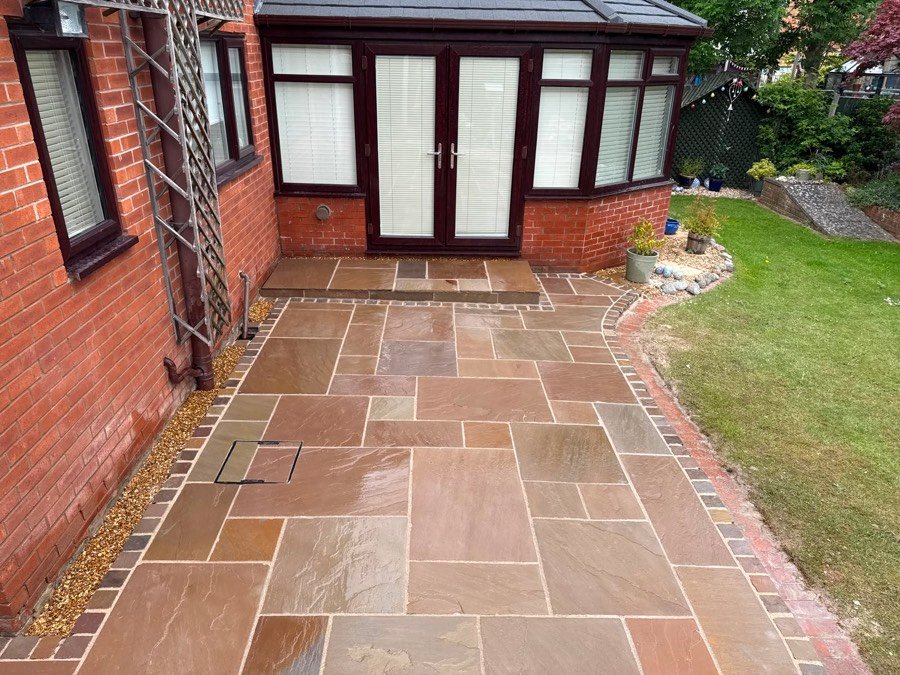 Autumn brown Indian sandstone patio with a curved brick sett border beside a conservatory in Wrexham